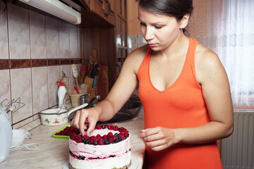 Young woman decorates a cake in the kitchen