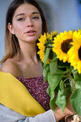 Young happy beautiful girl is walking in dress with a bouquet of sunflowers on a city street. Autumn concept