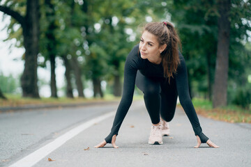 a confident woman of athletic build, standing in a stand before the start of the run, preparing to...