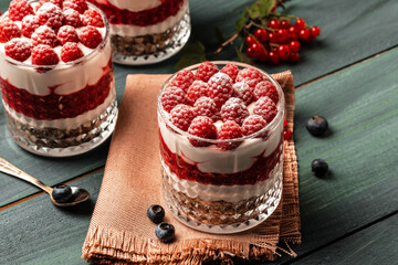 Healthy raspberry fruit dessert with skyr yogurt, granola layered in jar surrounded by ingredients, Vegetarian breakfast, fresh raspberries and blueberries yoghurt