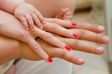 A family of three holds hand in hand. Baby's little hand on mom's and dad's hand.
