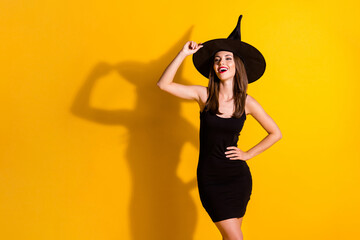 Photo of charming lovely selfish young lady hand hip hold cap scolding people make evil jokes fall theme event wear black witch costume cone headwear isolated yellow color background