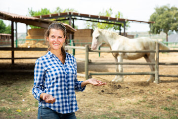 Happy confident young woman horses breeder standing near fencing of stable outdoors