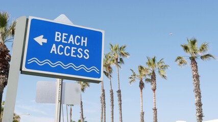 Fototapeta premium Beach sign and palms in sunny California, USA. Palm trees and seaside signpost. Oceanside pacific tourist resort aesthetic. Symbol of travel holidays and summertime vacations. Beachfront promenade