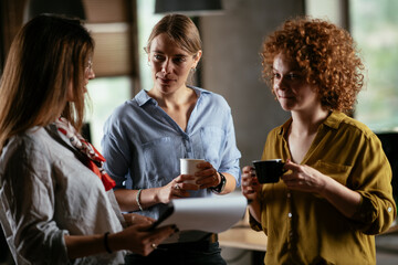 Girlfriends talking and laughing in office. Beautiful women drinking coffee in the office...