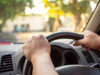 A man's hand held the steering wheel of a car to steer while the car was moving away. Concept and...