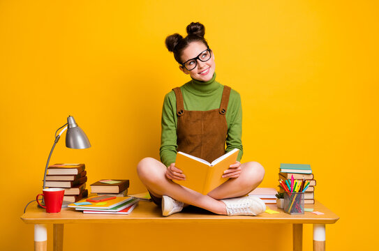 Full size photo of minded curious girl sit table legs crossed read book look copyspace think thoughts wear green jumper dress skirt overall isolated bright shine color background