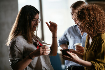 Girlfriends talking and laughing in office. Beautiful women drinking coffee in the office...