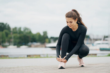Fototapeta premium a young woman of Caucasian appearance, brunette, cute, strong, confident. tying the laces on her athletic shoes.