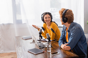 asian announcer in wireless headphones gesturing while talking to colleague in radio studio