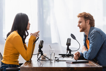 side view of young asian woman talking to redhead broadcaster during interview in studio