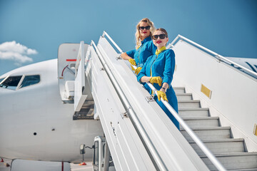Beautiful stewardesses standing on airplane stairs under blue sky