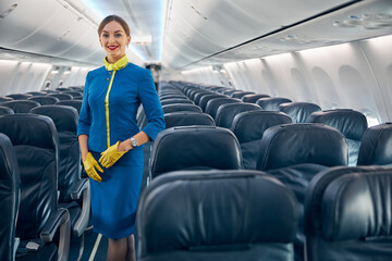 Young attractive woman in blue uniform posing at the photo camera in the salon of modern passenger aircraft