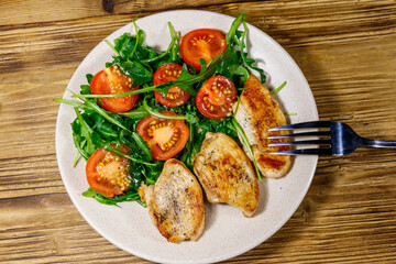 Fried chicken breast with salad of fresh arugula and cherry tomatoes on wooden table. Top view