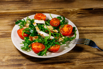 Tasty salad of fried chicken breast, fresh arugula and cherry tomatoes on wooden table