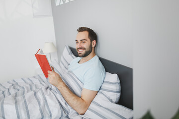Smiling pretty handsome young bearded man 20s wearing basic blue t-shirt hold in hands reading book...