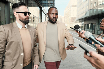 Serious businessman in sunglasses with his bodyguard giving an interview to journalists in the city