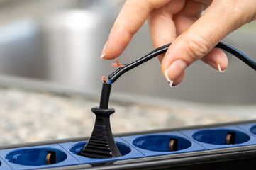 Close up of a woman hand holding a dangerous damaged electrical cord at kitchen