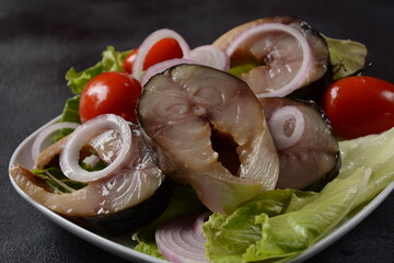 Sliced pieces of cold smoked mackerel fish, with cherry tomatoes,and red onion on lettuce leaves.