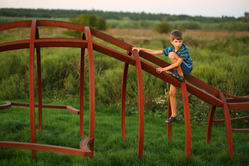 Obraz premium Sunset portrait of a thoughtful caucasian boy climbing at the outdoor modern playground