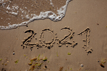 The numbers 2021 are written in the sand. New year on the beach. Sea coast, wave. Natural background. Place for your text. Summer in winter.