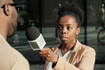African female journalist holding microphone and interviewing the man outdoors