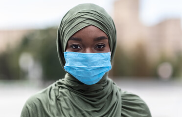 Portrait of black muslim woman wearing blue medical protective face mask outdoors