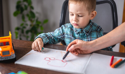 Mom is helping child to draw with pencils on paper in an album. Preschool education and development of creativity