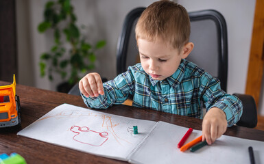Cute child boy draws with chalk on paper in an album at the table. Preschool education and development of creativity