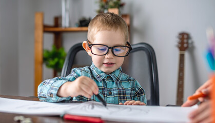 Cute child boy draws with chalk on paper in an album at the table. Preschool education and development of creativity