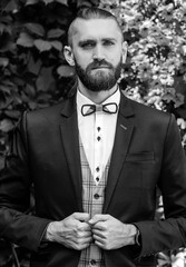 Fototapeta premium Black and white portrait bearded guy in a blue suit stands on the background of a flower wall