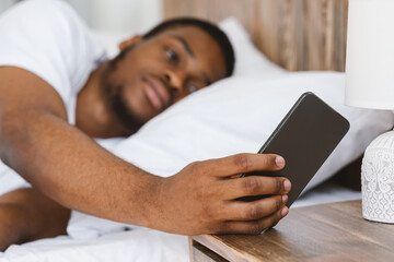 Black Man Turning Off Alarm-Clock Lying In Bed At Home