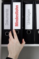 Mindestlohn. Ordner im Regal mit roter Beschriftung. Hand nimmt Dokumente aus Schrank im Büro