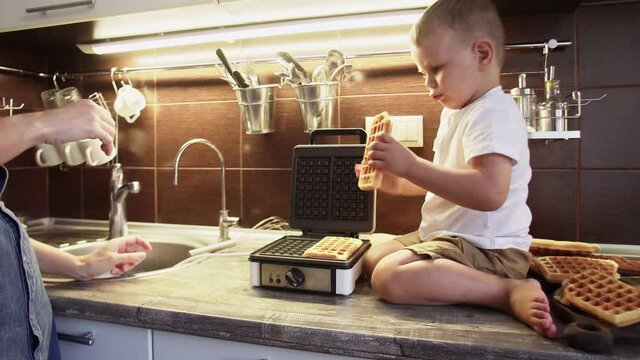 Close up of young mother and her son are making waffles in waffle maker at home kitchen