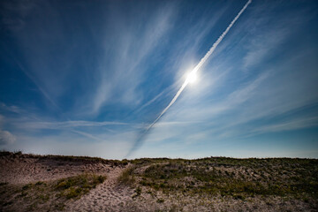 Naklejka na ściany i meble Sand dune on blue sky with sun and jet traces background. Estonia, Saaremaa, Harilaid nature reserve.
