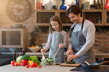 Little girl and her dad cooking healthy dinner together at home