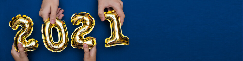 Hands up holding the Golden numbers 2021 from new year's balls of yellow metallic color on a blue background.The concept of a happy and healthy new year and Christmas. Banner