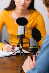 cropped view of broadcaster writing in notebook during interview with guest in studio