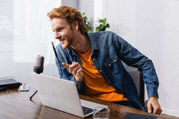 redhead broadcaster pointing with finger while speaking in microphone near laptop