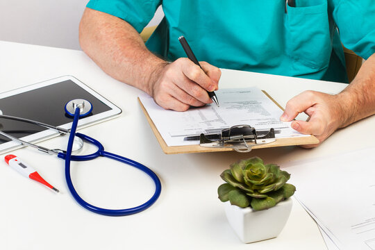 Médico escribiendo una prescripcion médica en su consulta junto a una tableta y un estetoscopio. Vista de frente y de cerca. Concepto: Salud