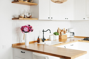 View on clean white simple modern kitchen in scandinavian style, aster Michaelmas daisy bouquet in vase on the table - obrazy, fototapety, plakaty