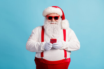 Fototapeta na wymiar Portrait of his he nice attractive cheery focused white-haired Santa using device gadget 5g app chatting blogging shop order isolated bright vivid shine vibrant blue color background
