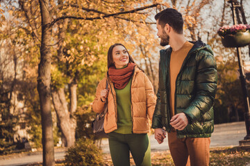 Photo of positive charming couple walk in fall forest town center park hold hands wear jackets backpack