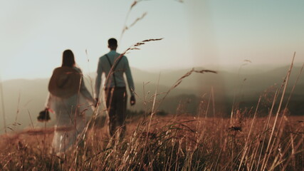 young couple in the mountains at sunset, in the foreground the grass