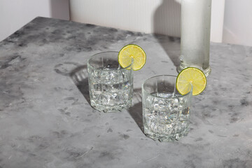 Vodka with ice and lime in two glasses and bottle of vodka on white background. Shadows and...