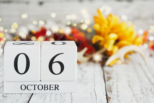 White wood calendar blocks with the date October 6th and autumn decorations over a wooden table. Selective focus with blurred background.
