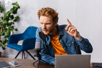 redhead announcer showing idea gesture while speaking in microphone near laptop