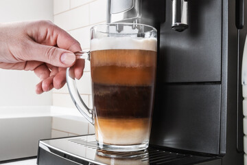 hand picks up a glass of cappuccino made in the coffee machine at home