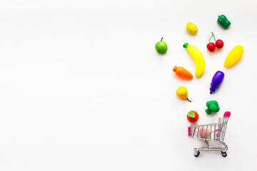 Concept of food and diet. Mini toy organic fruits and vegetables falling into mini shopping cart....