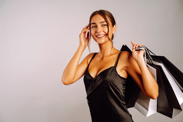 Elegant brunette woman in black dresse holding shopping bags. Young woman with black and white bags posing on grey background. Purchases, black friday, discounts, sale concept.